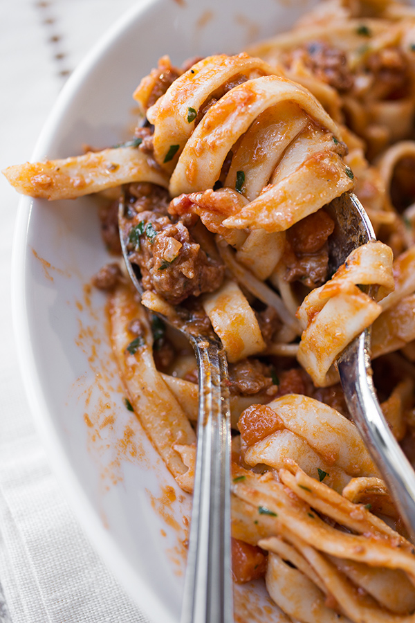 Fork in spoon filled with Fettuccine Bolognese with Sausage, resting on a plate | thecozyapron.com