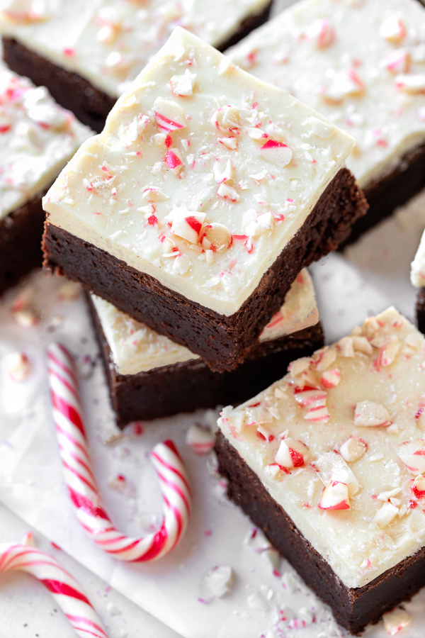 A small stack of freshly cut Peppermint Bark Brownies next to a candy cane | thecozyapron.com