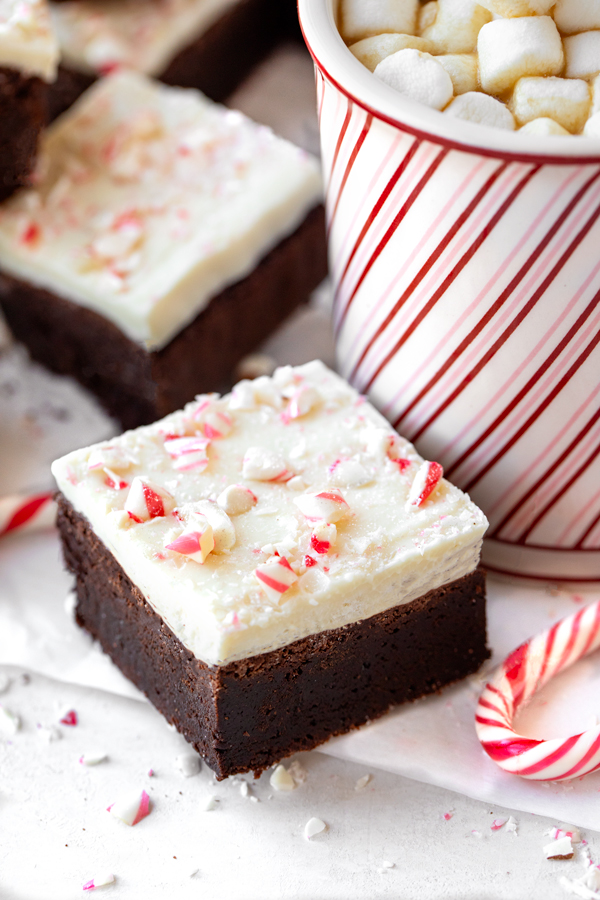 Closeup on a Peppermint Bark Brownie next to a cup of hot cocoa with marshmallows on top | thecozyapron.com