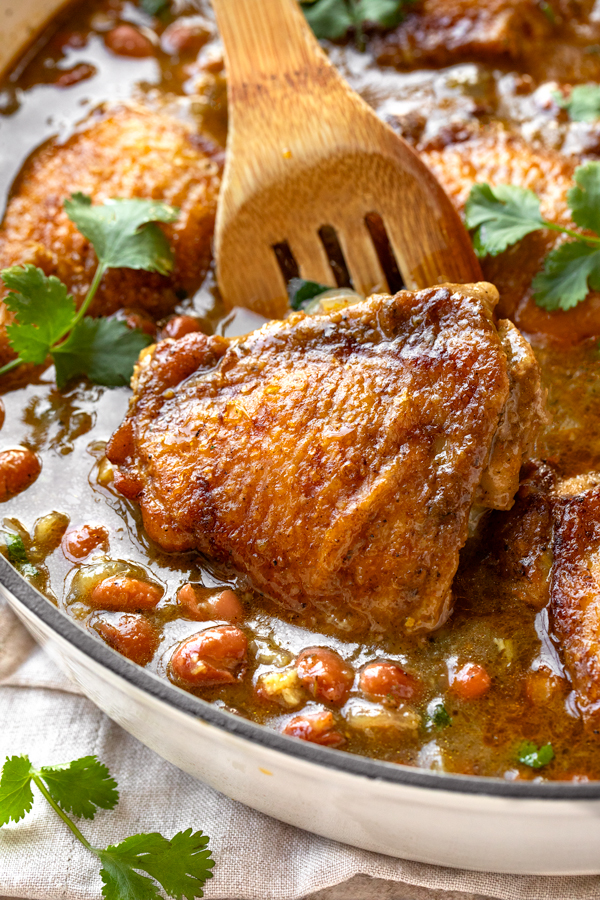 A piece of Salsa Verde Chicken with Beans being pulled out of a large braising pan | thecozyapron.com