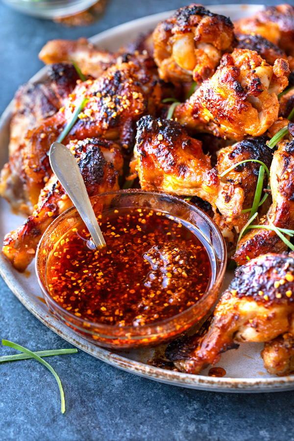 Closeup on a ramekin of Chili Crisp with a plateful of Spicy Chicken Wings | thecozyapron.com