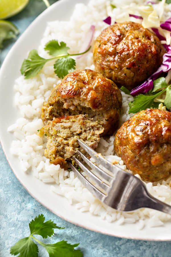 A closeup view of a Pork Meatball with Ginger and Lemongrass, on a bed of rice with Chili-lime slaw | thecozyapron.com