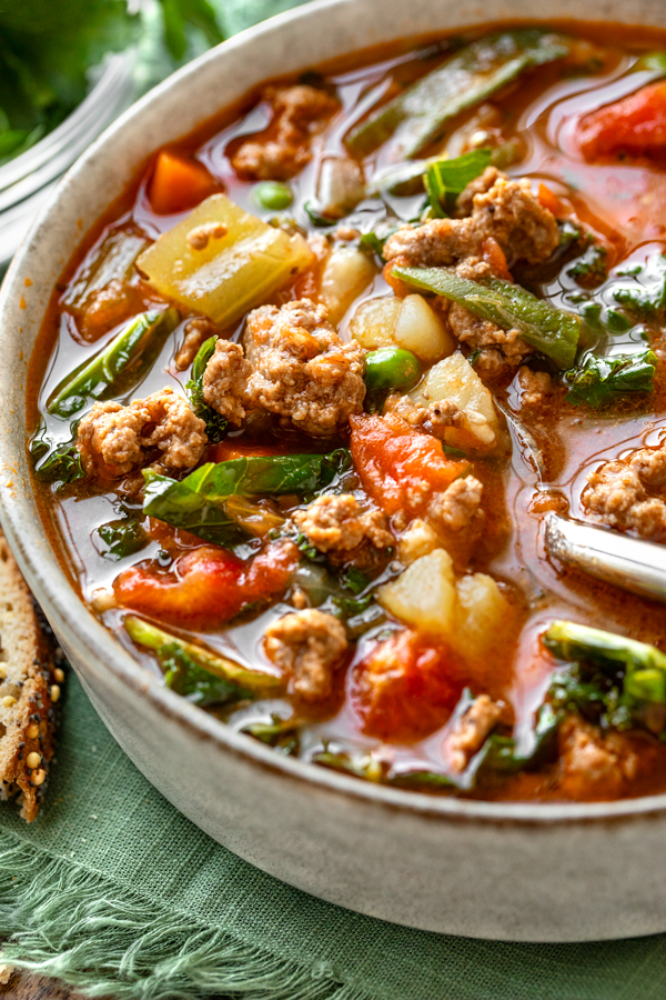 Close-up shot of a big bowl of Easy Vegetable Beef Soup with a few slices of bread | thecozyapron.com
