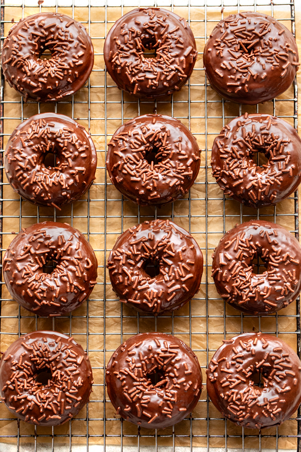 A dozen freshly baked Chocolate Glazed Donuts on a wire rack | thecozyapron.com