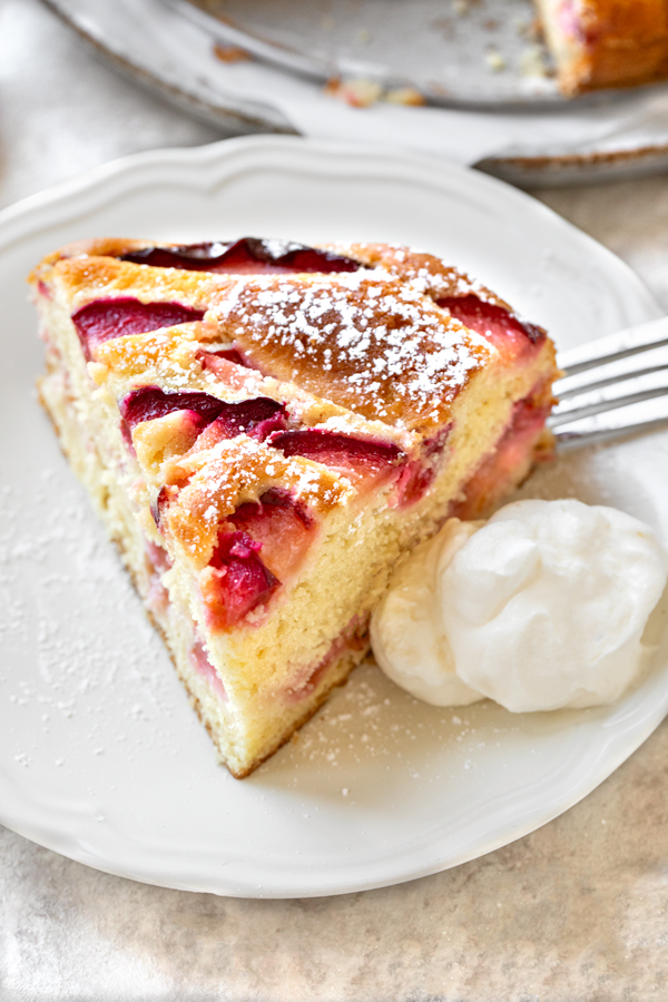 A fresh slice of Plum Cake served with a sprinkle of powdered sugar and a dollop of whipped cream on the side | thecozyapron.com