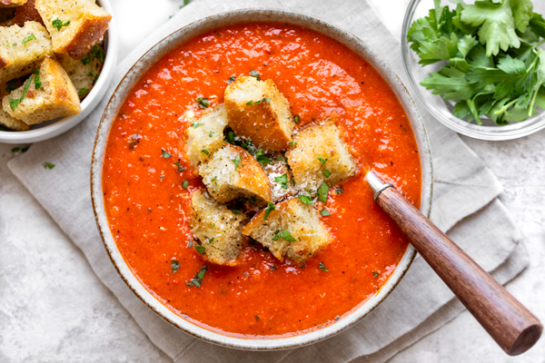 A bowl of Roasted Red Pepper and Tomato Soup, topped with crispy croutons | thecozyapron.com