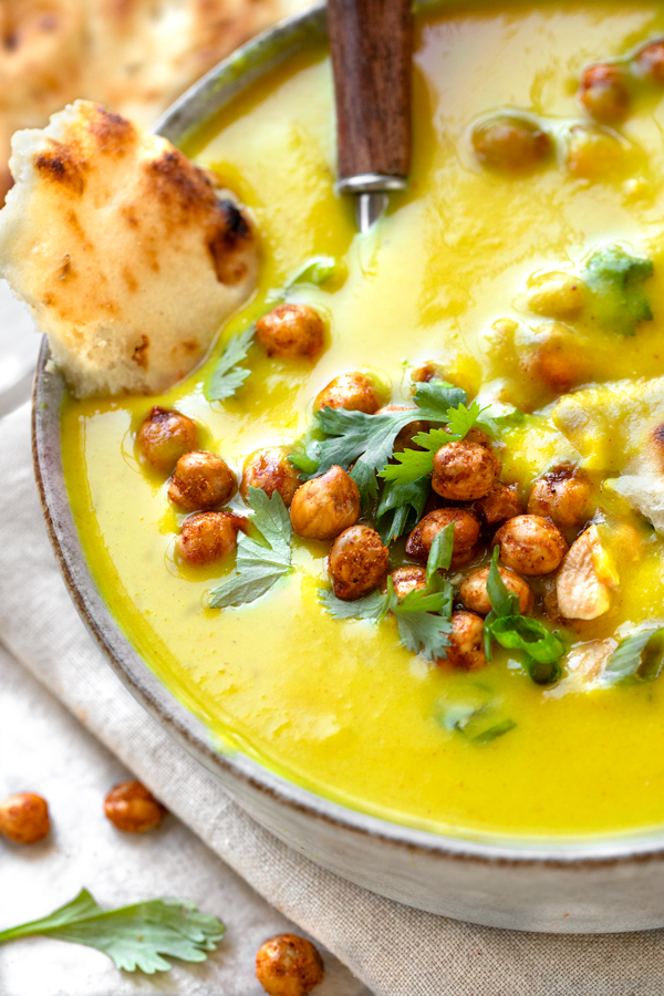 Closeup on a bowl of Golden Soup topped with crunchy chickpeas and cilantro, and with a side of naan | thecozyapron.com