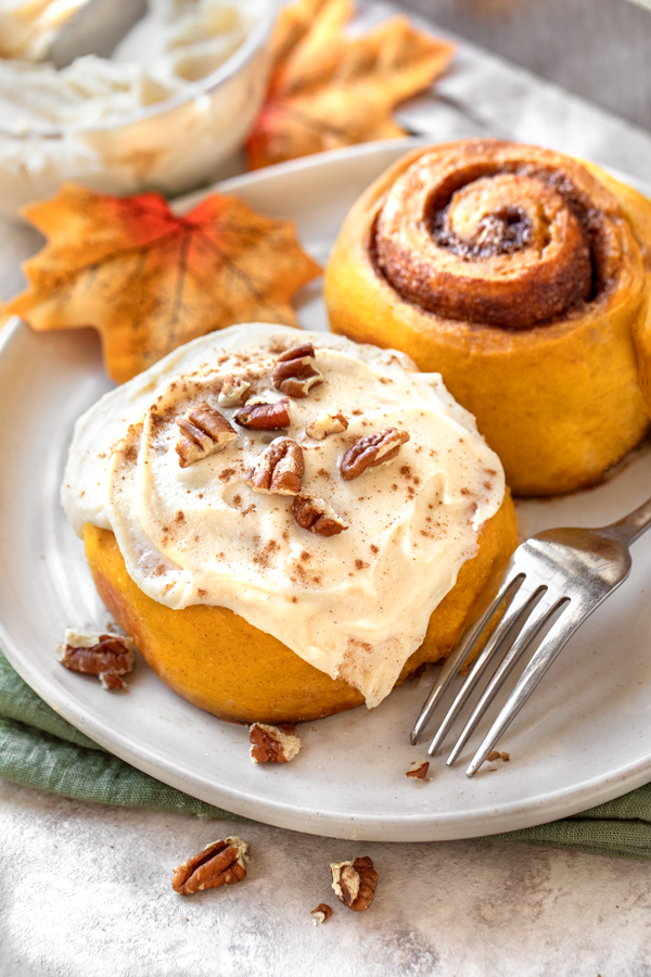 Two Pumpkin Cinnamon Rolls, one with frosting, one without | thecozyapron.com