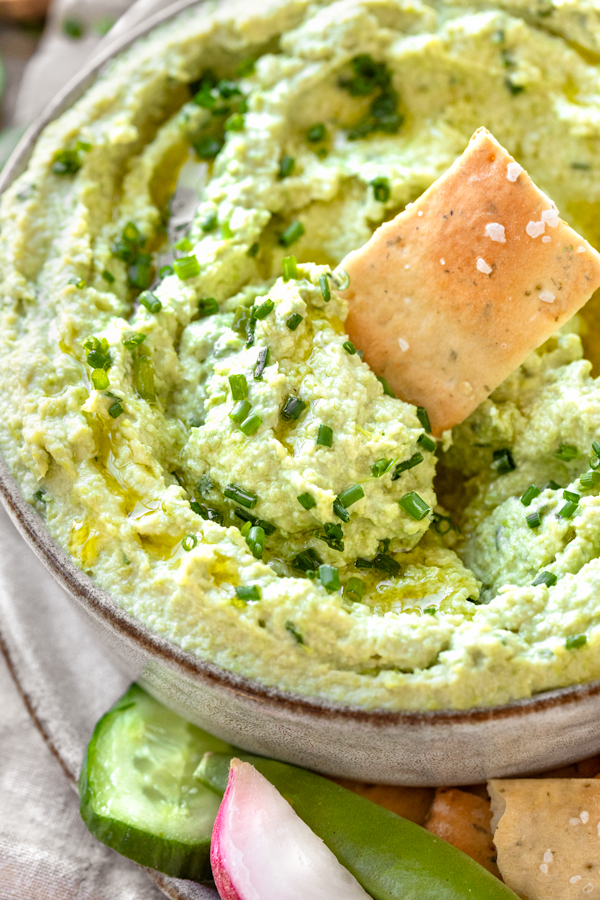 Closeup on a large bowl of freshly made Edamame Hummus, served with crackers and veggies | thecozyapron.com