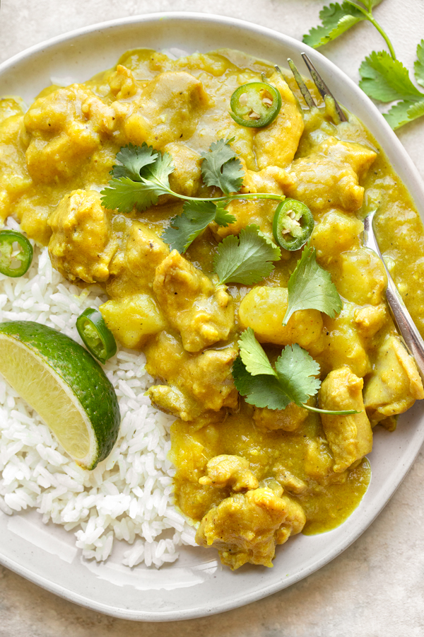 Overhead shot on a bowl of Coconut Curry Chicken over rice, topped with cilantro, peppers, and a lime wedge | thecozyapron.com