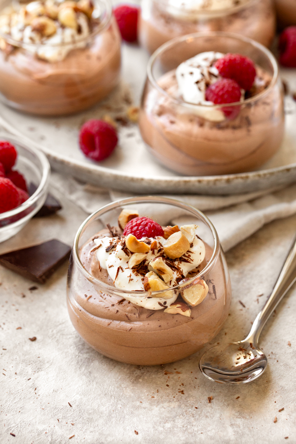 Closeup on a small glass filled with Easy Chocolate Mousse, topped with raspberries, toasted hazelnuts, and chocolate shavings | thecozyapron.com