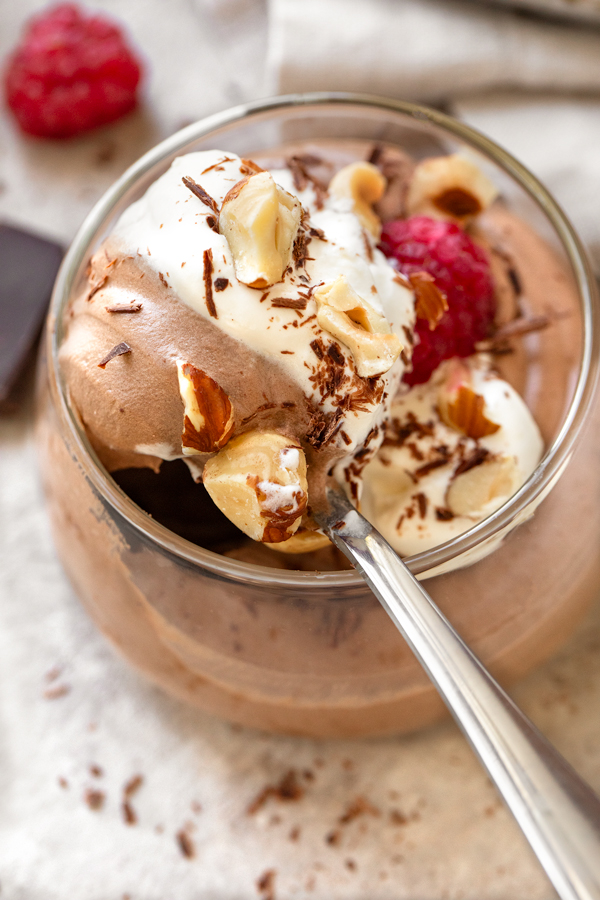 Closeup on a spoonful of Easy Chocolate Mousse, topped with raspberries, toasted hazelnuts, and chocolate shavings | thecozyapron.com