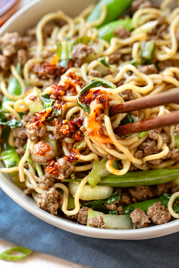 Closeup on chopsticks full of Beef Ramen Noodles with Snap Peas, and with chili crips on top | thecozyapron.com