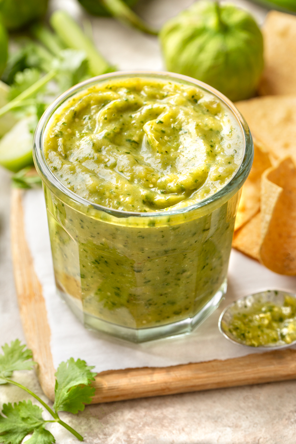 A jar of homemade Salsa Verde, with a few tortilla chips and a tomatillo in the background | thecozyapron.com