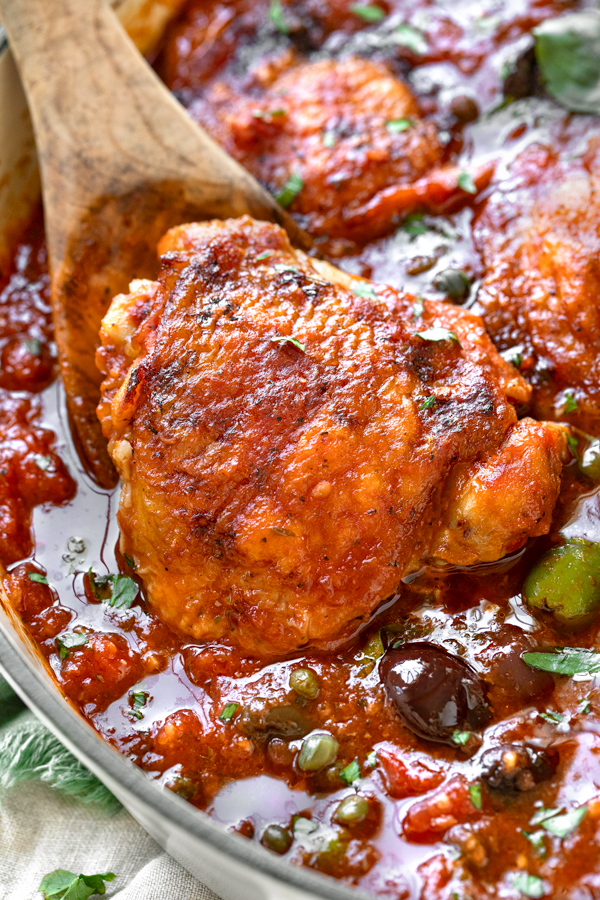 Closeup on a chicken thigh nestled in Puttanesca sauce | thecozyapron.com